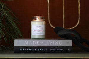 Tappen Apothecary Alpine Chateau scented candle on books with candleholder in background. Taken in Salmon Arm, British Columbia