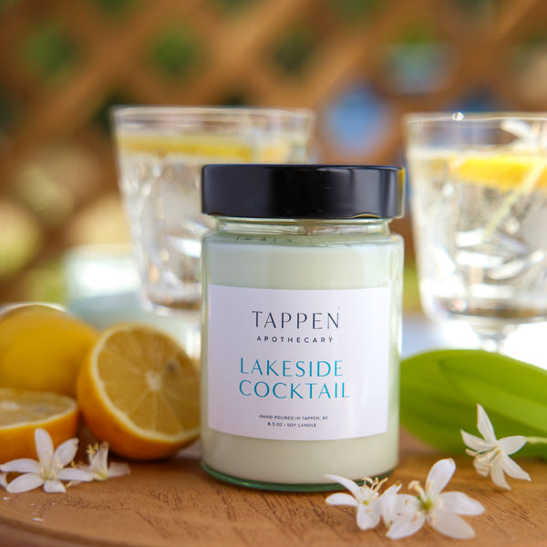 Tappen Apothecary Lakeside Cocktail on a wooden tray with lemons and flowers, outdoor setting.