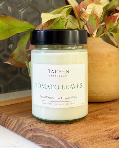 Jar of Tappen Apothecary Tomato Leaves candle on a wooden surface with leaves in the background